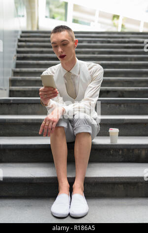 Young androgynous homosexual LGTB businessman sitting on stairs while using phone Stock Photo