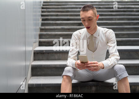 Young androgynous homosexual LGTB businessman sitting on stairs while using phone Stock Photo