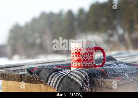 Steaming Cup of Hot Coffee or Tea standing on the Outdoor Wooden Table in Snowy Winter Day. Winter weekend or holidays, Christmas morning, healthy act Stock Photo