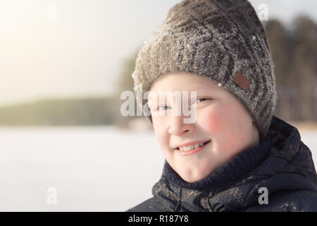 Cute teenage blond  boy in warm clothes, close up portrait on white snow, smiling outdoor in winter. Family weekend or holidays outside a city, winter Stock Photo