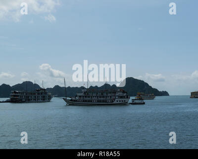 Junk boats tourist cruise in emerald waters of Halong Bay South China Sea Vietnam Asia with limestone island peaks covered in jungle foliage Stock Photo