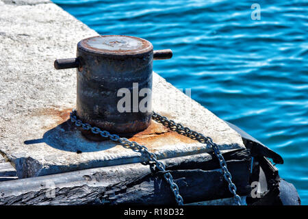 Old metal rusty mooring bollard with a chain wrapped around. Stock Photo