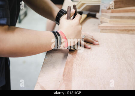 Thai engineer student prying nail from a wooden prank in carpentry workshop class. Stock Photo