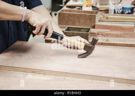Thai engineer student prying nail from a wooden prank in carpentry workshop class. Stock Photo