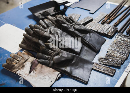 Fire Protection gloves, pliers and many pieces of steel on the desk to be used in electric metal welding workshop Stock Photo