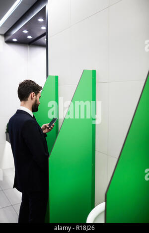 Mobile businessman in suit reading message or texting in smartphone while visiting wc Stock Photo