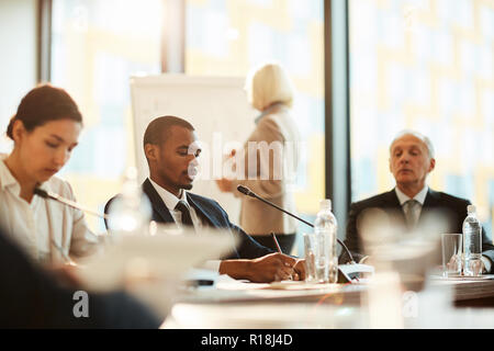 African-american delegate making working notes while sitting at conference among colleagues Stock Photo