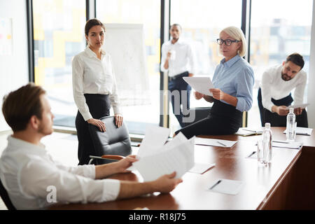 Female economists looking at one of colleagues while discussing financial papers at meeting Stock Photo