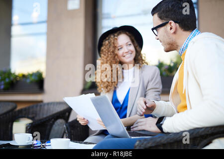 Young colleagues working with papers and discussing new ideas at working meeting in outdoor cafe Stock Photo