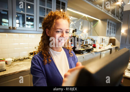 Pretty bar worker standing in front of computer and entering orders of clients Stock Photo