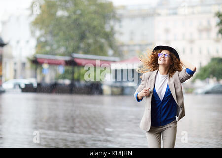 Happy young woman in casualwear running down boulevard in the rain Stock Photo