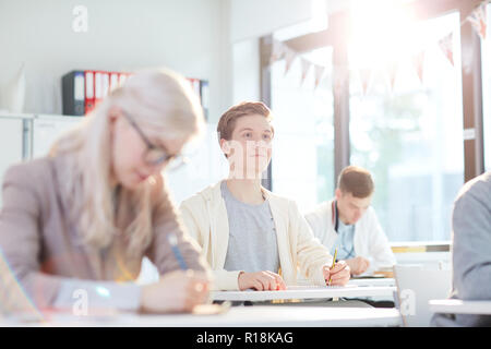 Clever guy looking at blackboard or listening to teacher while sitting by desk and making notes Stock Photo