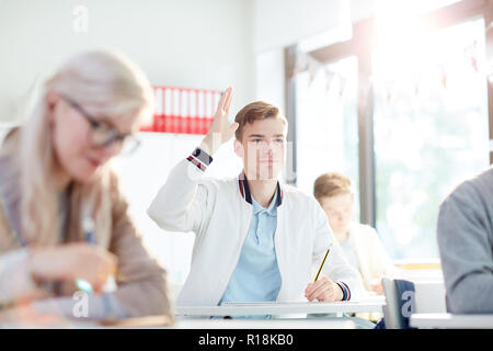 Smart guy in casualwear raising his hand to answer or ask question to teacher Stock Photo