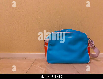 blue with red messenger school bag isolated in against a wall and standing on the floor in a room Stock Photo