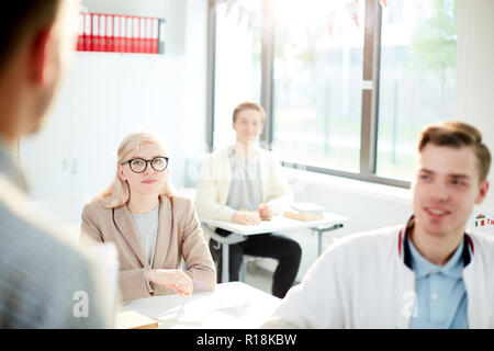 Attentive girl and two guys looking at their teacher during explanation of new subject Stock Photo