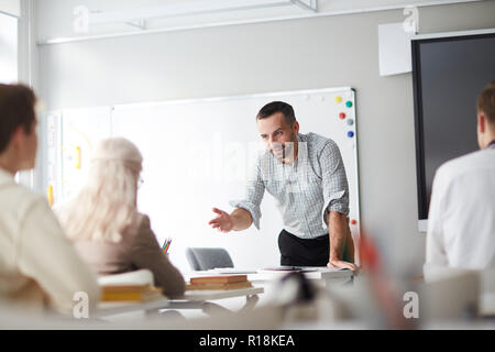 Confident teacher commenting one of students answer while explaining new topic Stock Photo