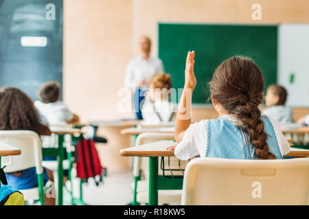 back view of schoolgirl raising hand to answer teachers question during lesson Stock Photo