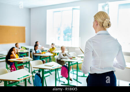 rear view of teacher looking at children sitting at classroom Stock Photo