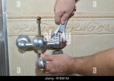 Man's hands with a plumber wrench starting to remove an old bathroom tap Stock Photo
