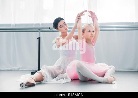 adult ballerina exercising with cute little child in pink tutu in ballet school