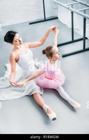 high angle view of adult ballerina exercising with cute little child in pink tutu in ballet school