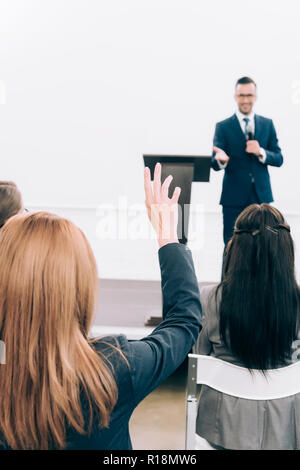 selective focus of lecturer talking in front of audience during seminar in conference hall, participant raising hand Stock Photo