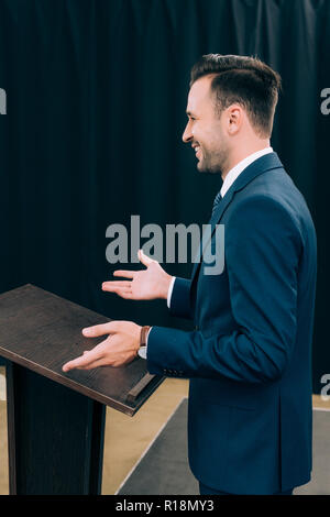 side view of handsome lecturer standing and gesturing at podium tribune during seminar in conference hall Stock Photo