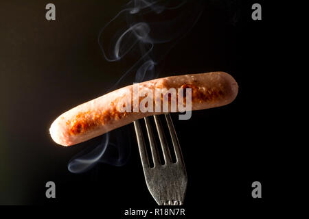 Grilled sausage on a fork fuming smoke dark black background Stock Photo