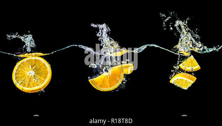 Composition of oranges falling into water close-up, macro, splash water, bubbles, isolated on a black background. Big large size. Stock Photo