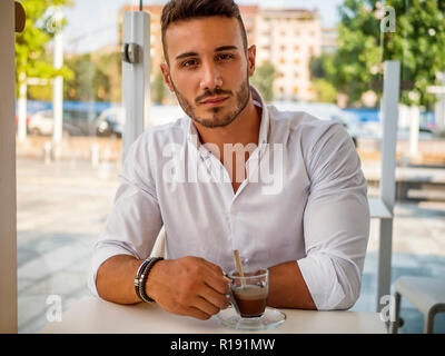 Attractive Young Man Drinking Coffee while Sitting in a Bar with Serious Expression Stock Photo