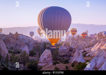 Hot air balloons flying in beautiful Cappadocia hilly landscape, amazing tourism attraction in Goreme, Anatolia, Turkey, morning sun light Stock Photo
