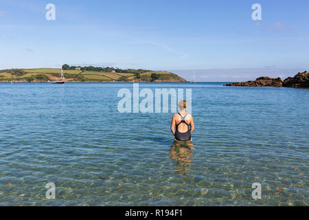 Woman wearing a swimming costume entering the cool, clear water at Bosahan Cove on the the Helford River Estuary in Cornwall, England. Stock Photo