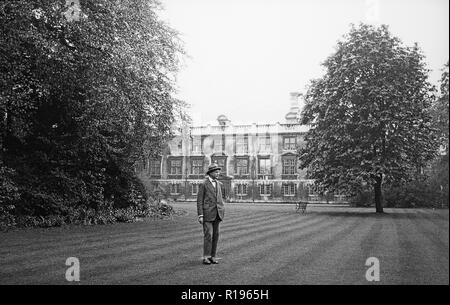 A vintage black and white photograph, taken in May 1924, showing  a man standing in a garden with the Fellow's Building, part of Christ's College, Cambridge University, England, in the background.
