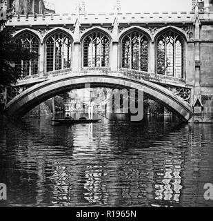 Black and white vintage photograph taken in 1924 showing the Bridge Of Sighs, a covered bridge at St.John's College, Cambridge, England. It was built in 1831 and crosses the River Cam between the college's Third Court and New Court. The architect was Henry Hutchinson. Photo shows a couple in punt, the traditional boat used on the river, with a man standing and using a pole. Stock Photo