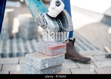 Builder in uniform cutting paving tiles with electric cutter, close-up view Stock Photo