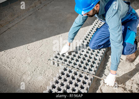 Builder laying paving tiles with holes for grass on the construction site, view from above Stock Photo