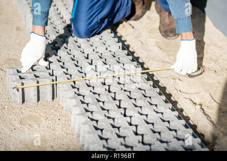 Builder measuring paving tiles with holes for grass on the construction site, close-up view from above Stock Photo