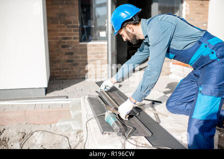 Builder in uniform measuring metal window sills for cutting on the construction site Stock Photo