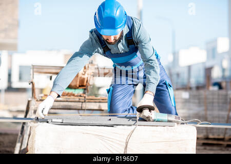 Builder in uniform measuring metal window sills for cutting on the construction site Stock Photo