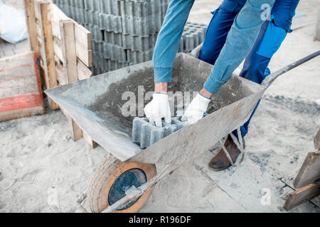 Builder loading paving tiles into the pushcart standing on the construction site, close-up view with no face Stock Photo