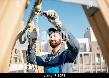 Handsome workman in uniform mounting swing on the playground outdoors Stock Photo