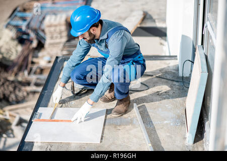 Workman in uniform mounting ceramic tiles on the balcony at the construction site Stock Photo