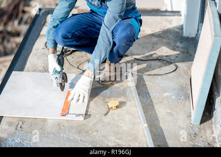 Workman in uniform mounting ceramic tiles on the balcony at the construction site Stock Photo