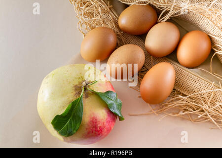 Six eggs and one pomegrenate on a brown sackcloth (burlap) and white background- traditional organic food concept demonstration Stock Photo