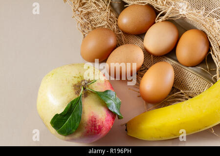 Six eggs one pomegrenate and one banana on a brown sackcloth (burlap) and white background- traditional organic food concept demonstration Stock Photo