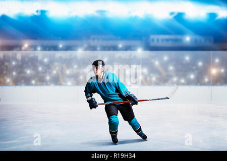 A hockey player on ice in action, arena spotlights and tribunes with fans on background. Male person in helmet, gloves and uniform holds stick in hand Stock Photo