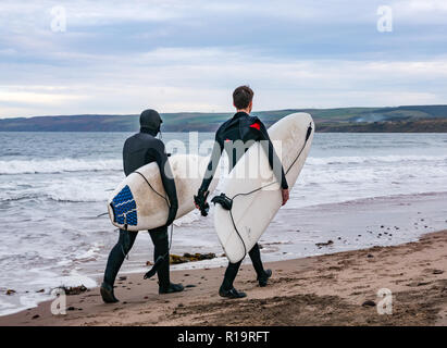 Torness, East Lothian, Scotland, United Kingdom, 10th November 2018. UK Weather: Despite the storm on the UK's West coastline, Eastern Scotland is mild with only a slight breeze. A surfer couple walk onto the beach carrying surf boards at Thorntonloch to go surfing Stock Photo