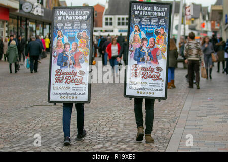 Double-sided poster display Blackpool, Lancashire, UK. 10th Nov, 2018. Sandwich theatre board advertising Beauty & The Beast pantomime, Carried by a person, with one board in front and one behind in a triangle shape; Shoppers, shopping and shops on a busy Christmas shopping day in the resort. C Stock Photo