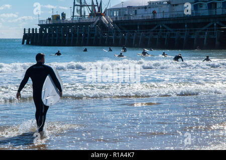 Surfers in the sea on Bournemouth beach in high summer, below the famous pier Stock Photo