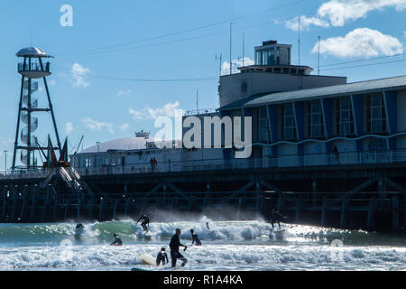 Surfers in the sea on Bournemouth beach in high summer, below the famous pier Stock Photo